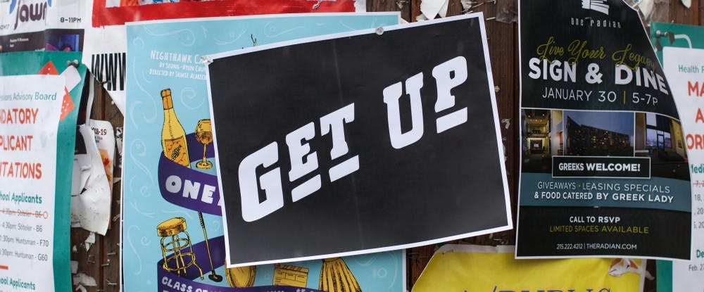 Photo shows a black paper sign with white lettering that reads "GET UP" on a bulletin board with other posters. Photo courtesy The DG