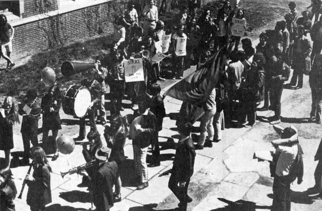 Antiwar demonstrators following the Penn marching band during Hey Day in 1972. Students rallied to protest the U.S.'s involvement in the Vietnam War and Penn's role in funding the war effort. In a black and white photo, students with signs and a megaphone confront band members playing their instruments. Photo courtesy of Penn Archives.